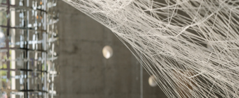 Oeuvre d'art constituée de fils blancs pendus à des crochets, sur font gris foncé
