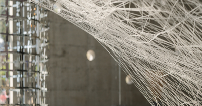Oeuvre d'art constituée de fils blancs pendus à des crochets, sur font gris foncé