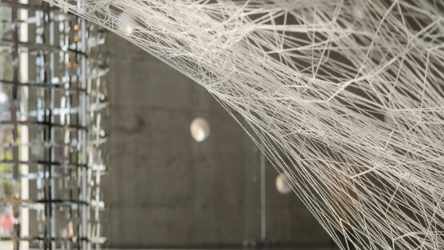 Oeuvre d'art constituée de fils blancs pendus à des crochets, sur font gris foncé